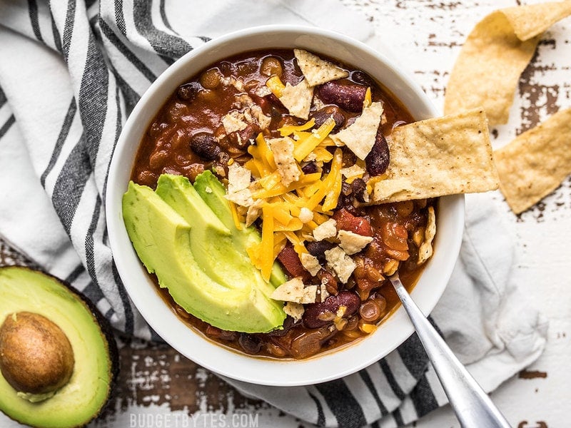This Slow Cooker Vegetarian Lentil Chili makes a huge batch, is packed with flavor and nutrients, and can be made for only about 5 dollars! Budgetbytes.com A bowl of Slow Cooker Vegetarian Lentil Chili with avocado and tortilla chips