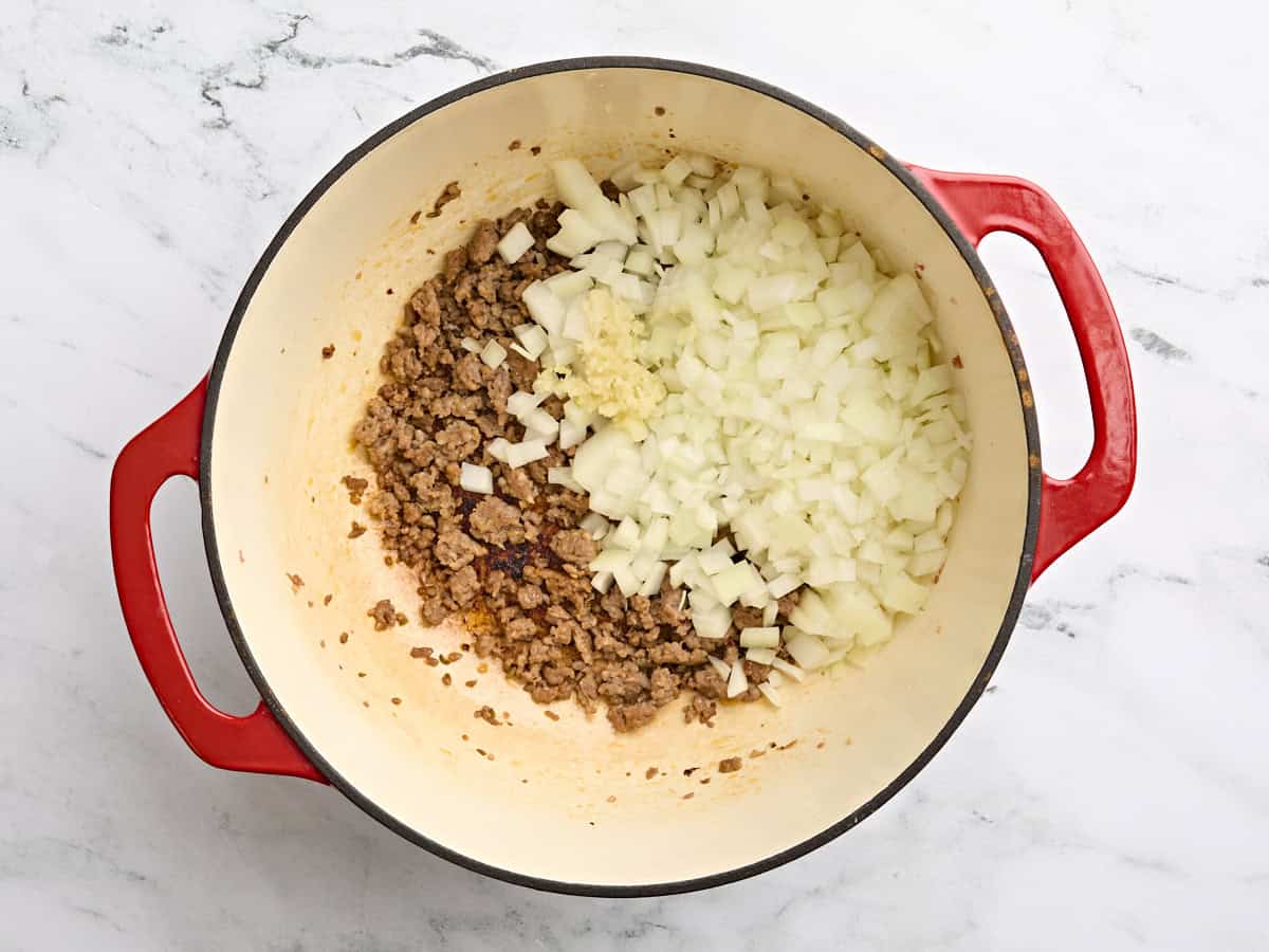 Ground Italian sausage in a soup pot with diced onions.