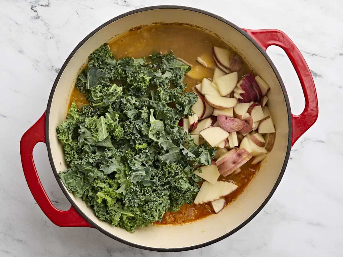 Sliced potatoes and kale added to a pot of zuppa toscana.