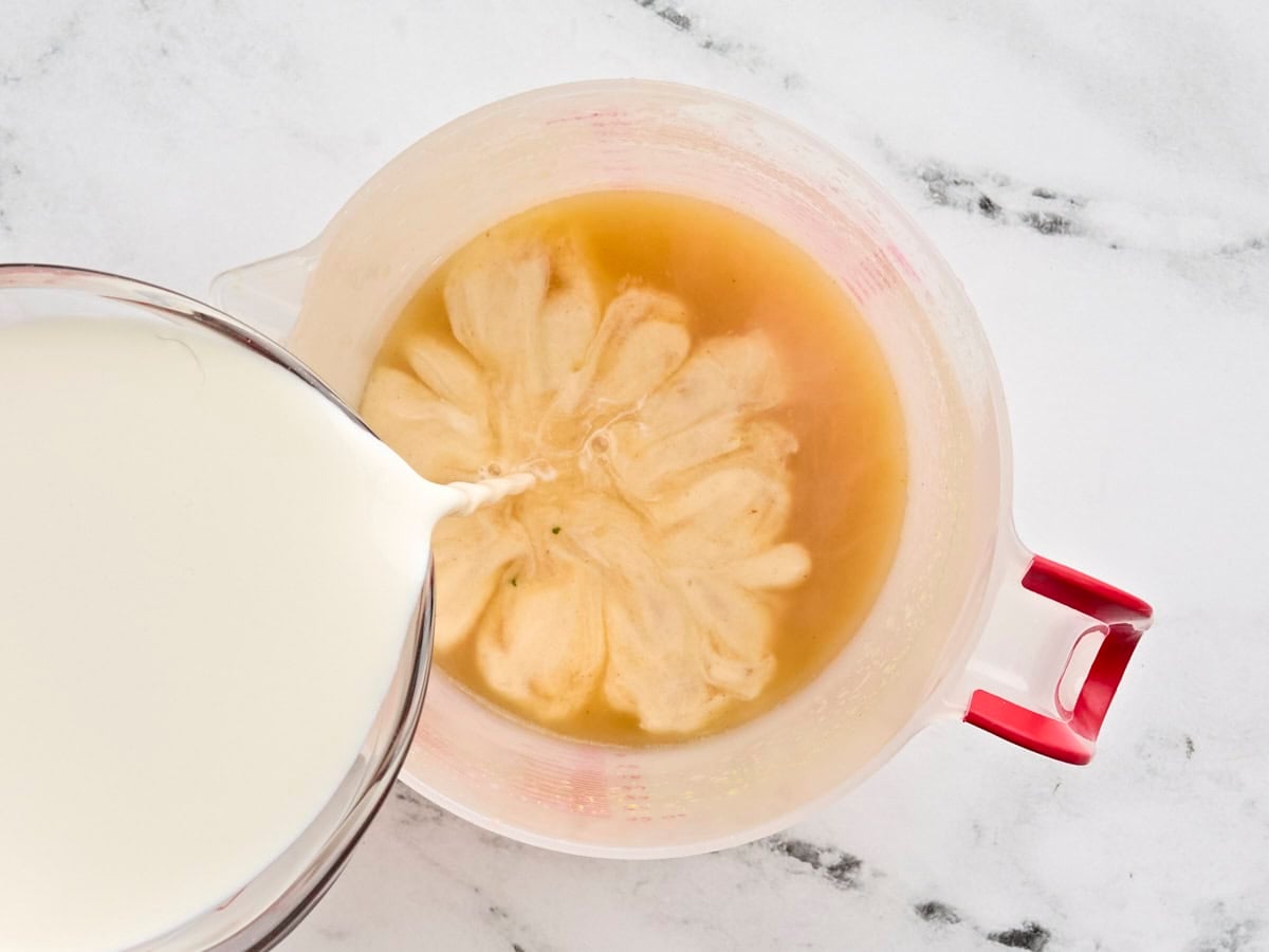 A jug of hot broth, with half and half being poured into it to temper.