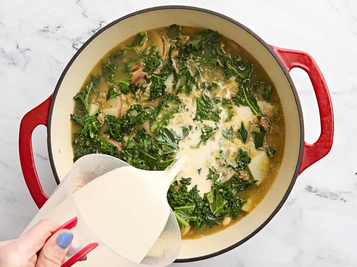 A tempered half and half and chicken broth mixture being poured into a pot of zuppa toscana.