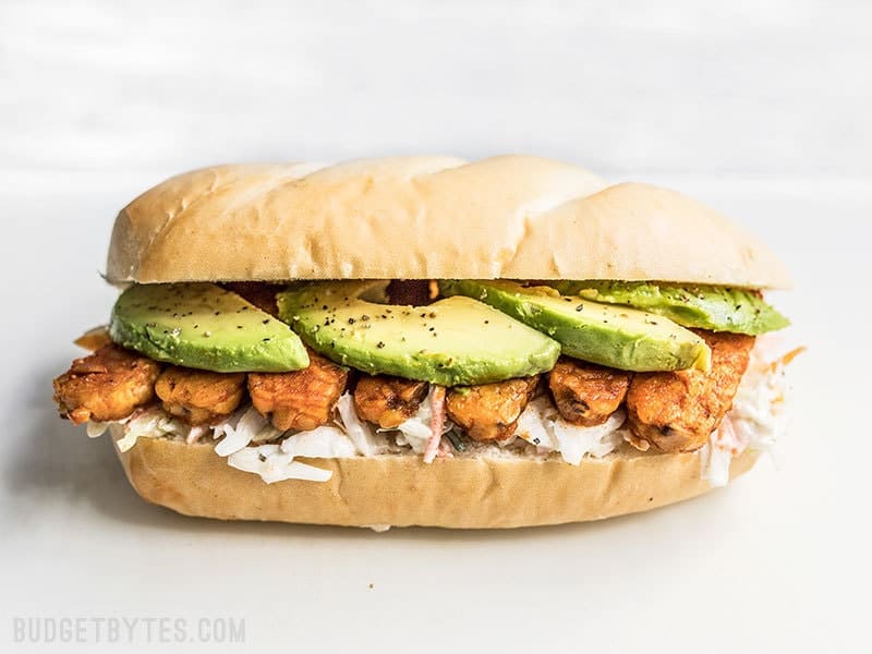 Spicy hot buffalo sauce, creamy avocado, and a rich and tangy ranch slaw makes these Buffalo Tempeh Sandwiches fiery perfection! Budgetbytes.com Buffalo Tempeh Sandwich on a Cutting Board