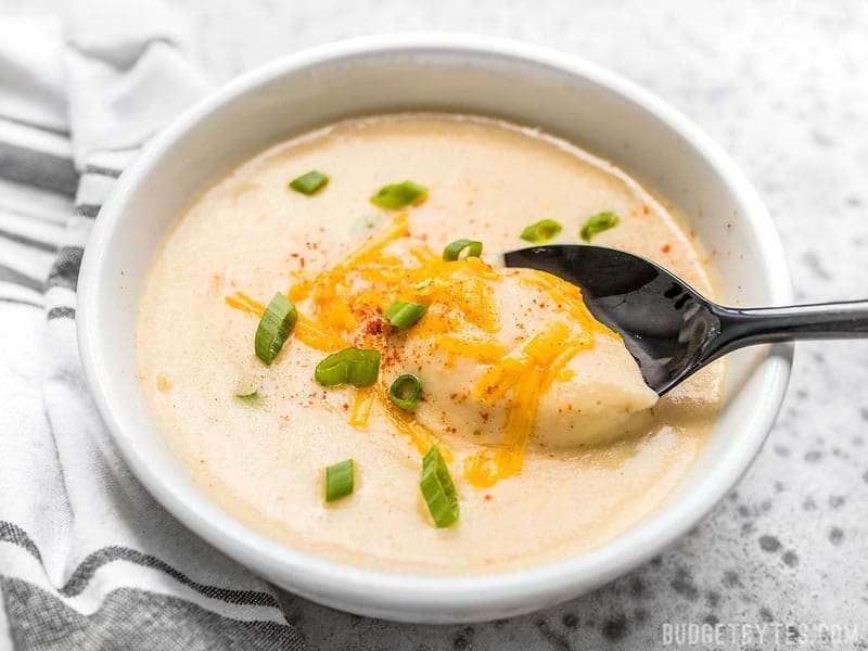 Cheesy Cauliflower and Potato Soup is rich and creamy without being overly heavy. Eat your vegetables and enjoy them, too! Budgetbytes.com A spoon scooping Cheesy Cauliflower and Potato Soup out of a bowl