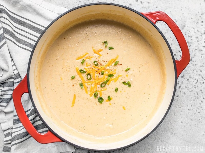 Cheesy Cauliflower and Potato Soup is rich and creamy without being overly heavy. Eat your vegetables and enjoy them, too! Budgetbytes.com A finished pot of Cheesy Cauliflower and Potato Soup with cheddar and green onion sprinkled on top.