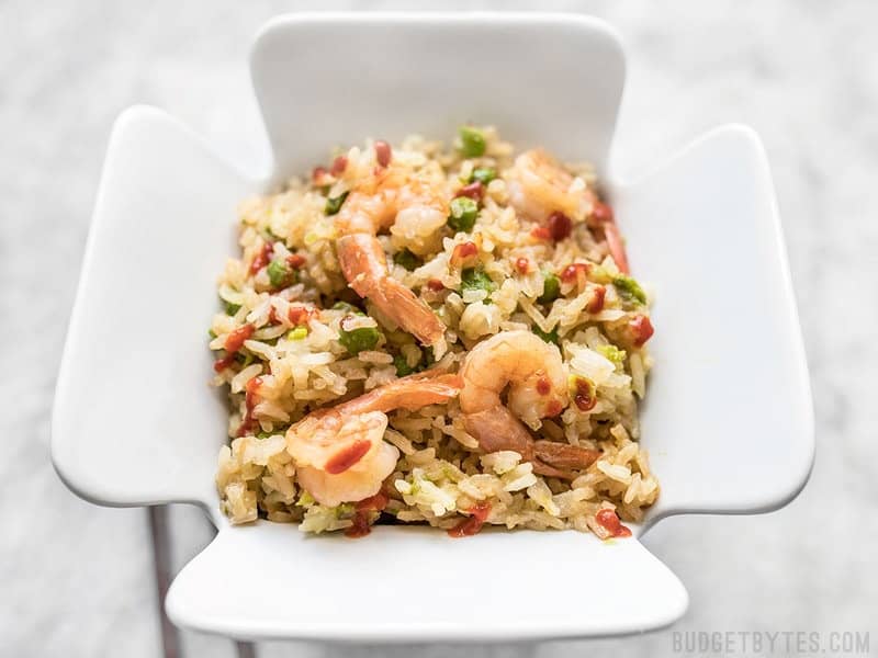 By adding a few extra ingredients to your rice cooker, you can cook an entire meal at once. This Teriyaki Shrimp and Rice is an easy and healthy alternative to take out. Budgetbytes.com Rice Cooker Teriyaki Shrimp and Rice in a white ceramic take out container.