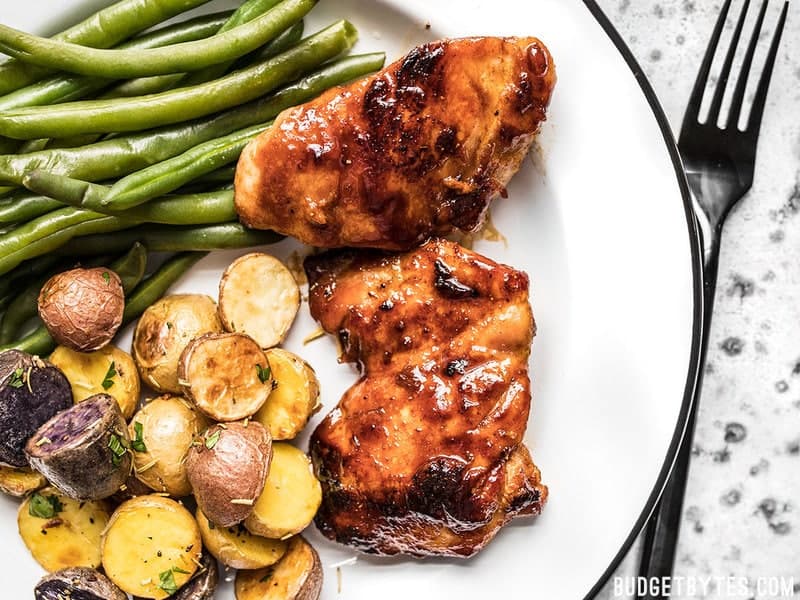 Sweet and Spicy Glazed Chicken Thighs on a plate with rosemary roasted potatoes and steamed green beans.