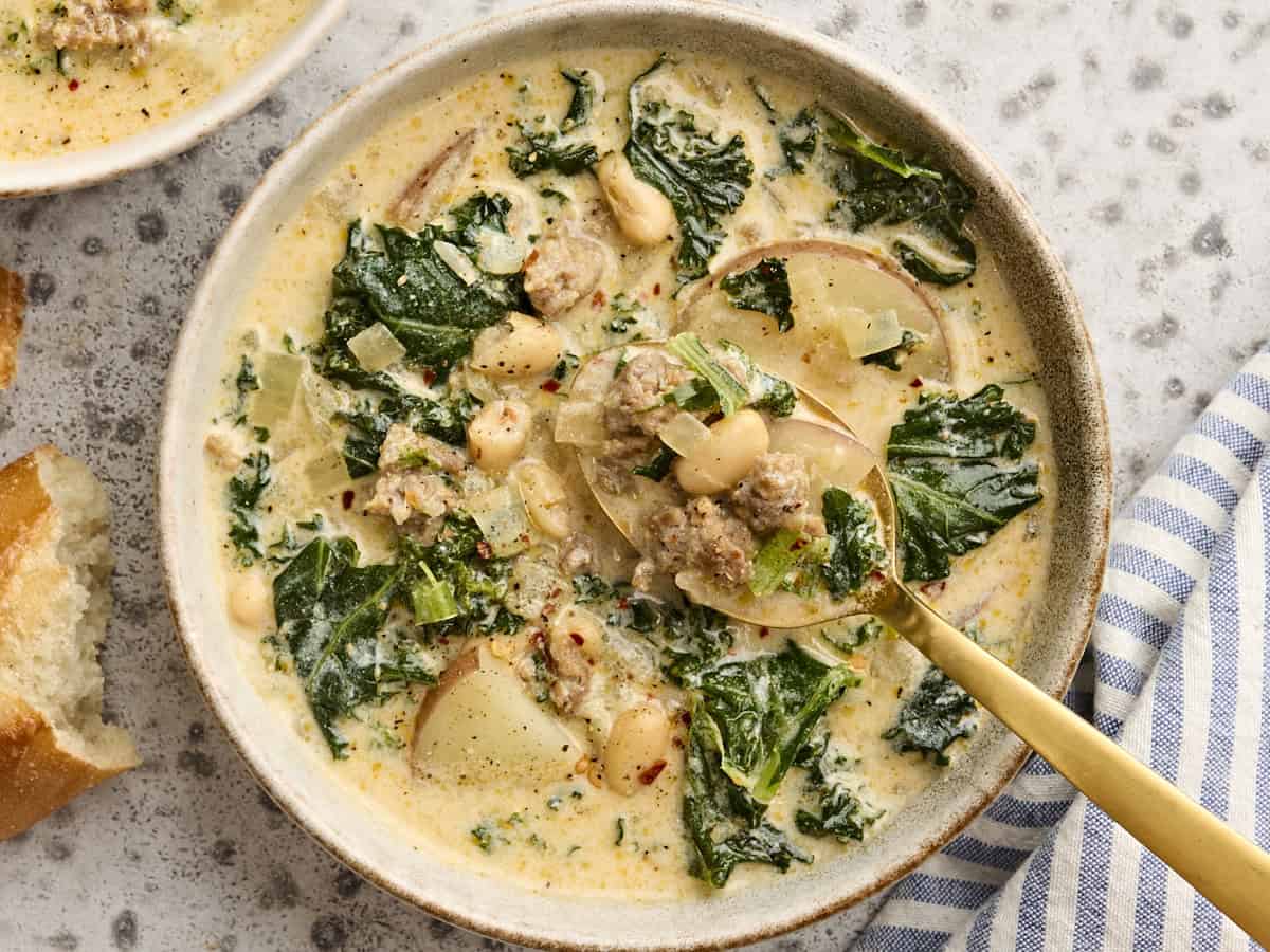 Overhead view of a bowl of zuppa toscana with a spoon taking some.