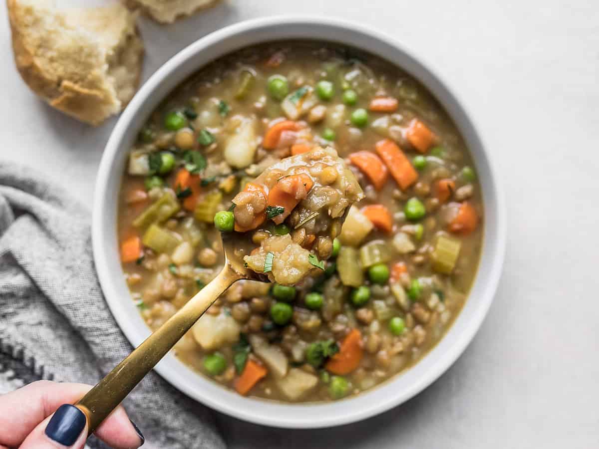 A rich and hearty medley of vegetables, lentils, and herbs makes this freezer-friendly Vegan Winter Lentil Stew the perfect cold-weather comfort food. Budgetbytes.com A hand lifting a spoonful of lentil stew out of the bowl.