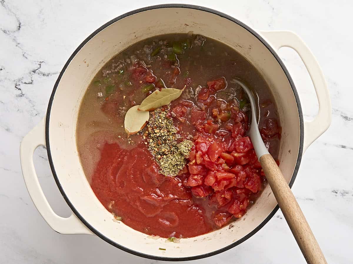 Canned diced tomatoes, tomato sauce, soy sauce, and seasonings added to a soup pot with browned ground beef and vegetables.