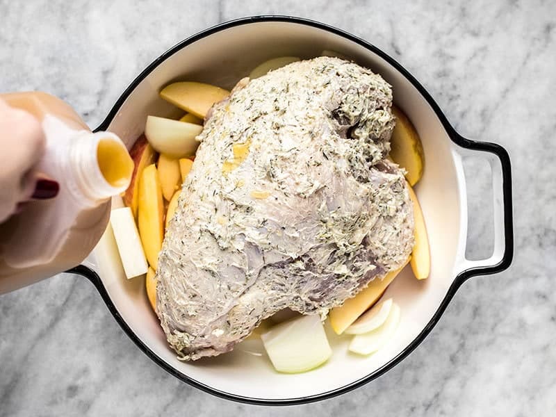 Apple cider being poured into a casserole dish with turkey breast, apples, and onions.