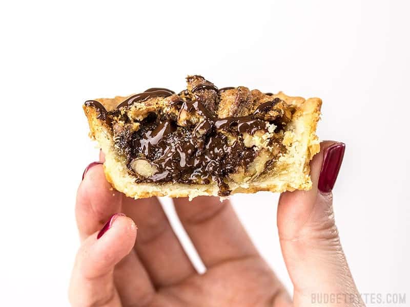 These easy Mini Pecan Pies studded with dark chocolate make the perfectly balanced and pre-portioned dessert for all of your holiday gatherings. Budgetbytes.com Close up of a Mini Dark Chocolate Pecan Pie cut in half.