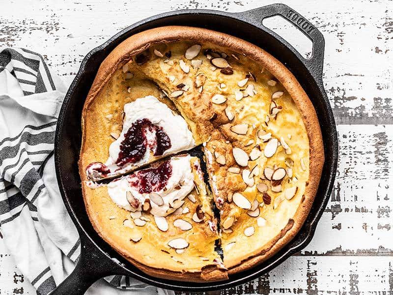 This Almond Dutch Baby with Ricotta and Jam is an easy way to dress up a lazy weekend brunch at home. Customize the add-ins and toppings to fit your mood! Budgetbytes.com Almond Dutch Baby with Ricotta and Jam sliced and ready to serve