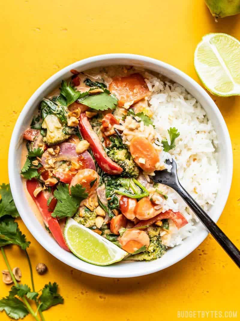 This rich and spicy coconut vegetable stir fry is adaptable to whatever vegetables are lingering in your fridge, making it a great sweep the kitchen recipe! Budgetbytes.com Big bowl of Spicy Coconut Vegetable Stir Fry with lime wedge