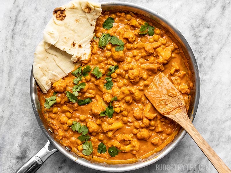 This super easy, ultra creamy, and heavily spiced Cauliflower and Chickpea Masala will be your new favorite weeknight dinner! So much flavor, so little effort. Budgetbytes.com Finished skillet full of Cauliflower and Chickpea Masala with cilantro and torn pieces of Naan bread