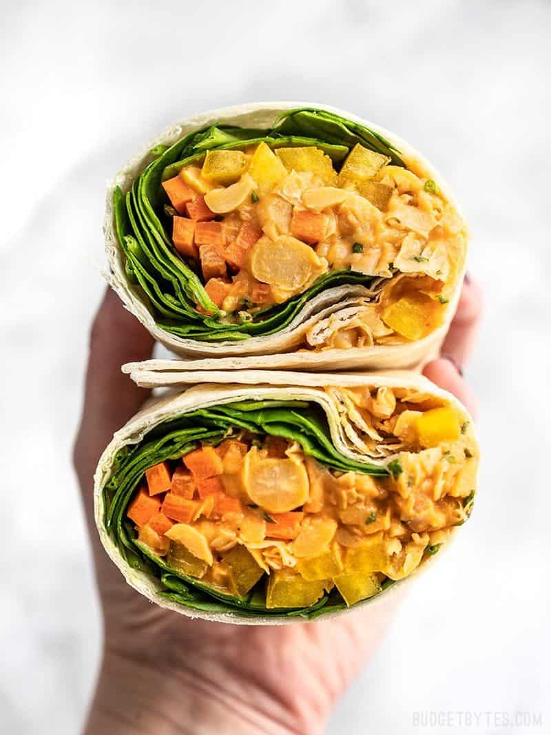 Creamy, spicy, and filling, these Sriracha Chickpea Salad Wraps are an easy option for your brown bag lunch. Customize to use whatever vegetables you have! Budgetbytes.com A Sriracha Chickpea Salad Wrap cut open, with open sides facing viewer.