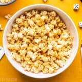 A big white bowl of Sriracha Nooch Popcorn next to dice and other game pieces