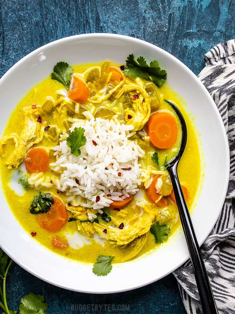 Warm, earthy, creamy and delicious! This Coconut Turmeric Chicken Soup is a fun twist on your comforting classic homemade chicken soup. Budgetbytes.com A big bowl of Coconut Turmeric Chicken Soup topped with rice and cilantro.