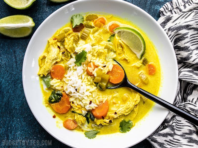Warm, earthy, creamy and delicious! This Coconut Turmeric Chicken Soup is a fun twist on your comforting classic homemade chicken soup. Budgetbytes.com Coconut Turmeric Chicken Soup being eaten with rice and cilantro