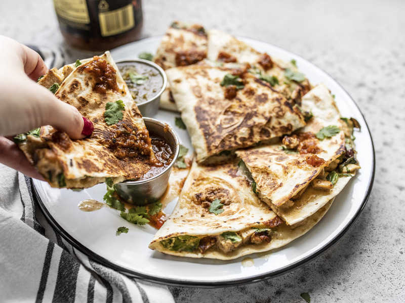 These Creamy Chicken and Spinach Quesadillas are seriously simple, but still deliciously dinner-worthy. Perfect for busy weeknights or picky eaters! Budgetbytes.com A hand dipping a piece of Creamy Chicken and Spinach Quesadillas into a dish of salsa