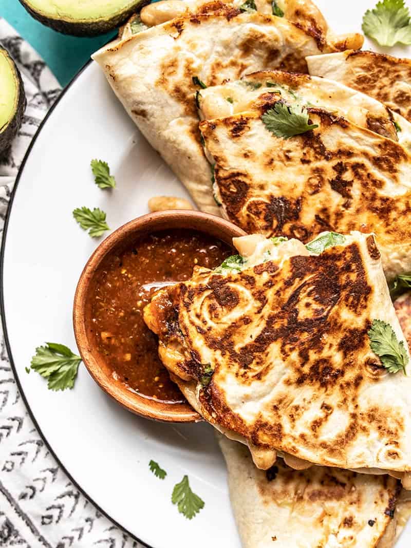 Crispy on the outside, creamy on the inside, these insanely delicious Creamy White Bean and Spinach Quesadillas make an awesomely fast weeknight dinner. Budgetbytes.com Close up of a quesadilla being dipped into a bowl of red salsa