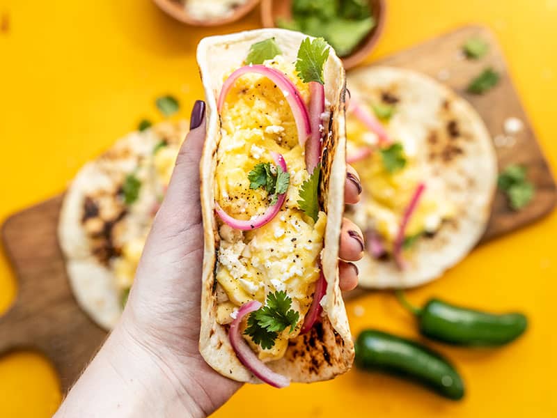 Hummus Breakfast Tacos are a quick and easy, protein and fiber packed breakfast that will keep you fueled all morning. Customize the toppings as desired! Budgetbytes.com One Hummus Breakfast Taco being held close up to the camera with the other two in the background
