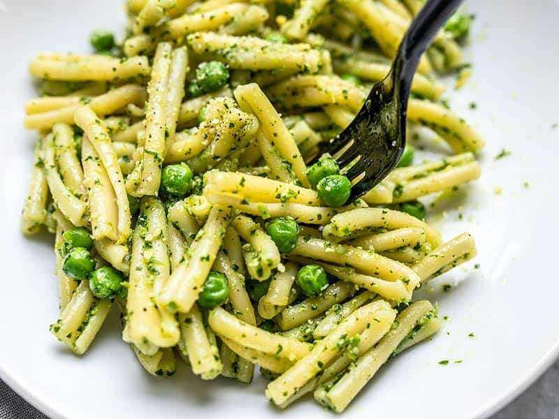 Parsley Pesto Pasta with Peas has super bright and fresh flavors perfect for spring and summer. Serve as a main dish or a side with your grilled food. Budgetbytes.com Close up of a black fork picking up some Parsley Pesto Pasta with Peas out of a bowl