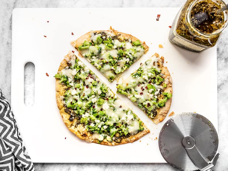 This "Quick Fix" Broccoli Pesto Pizza is the fastest and easiest route to getting your pizza fix, with an extra thin and crispy tortilla crust. Budgetbytes.com Sliced Quick Fix Broccoli Pesto Pizza on a cutting board with a jar of pesto and pizza wheel on the side.
