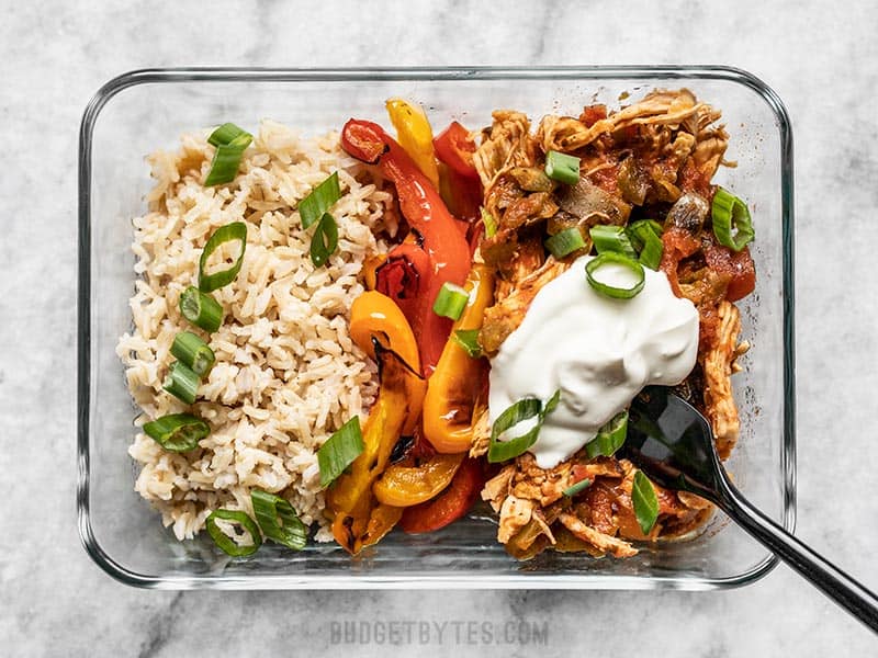 These easy Salsa Chicken Meal Prep Bowls are easy to customize to fit your diet or macros, and are 1/3 the cost of a meal delivery service. Budgetbytes.com Salsa chicken meal prep container close up, topped with green onion and sour cream