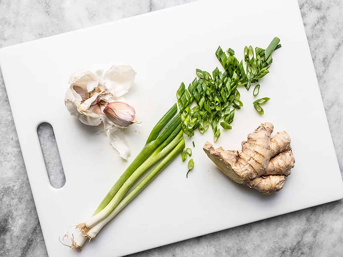 Garlic, green onion, and fresh ginger on a cutting board.