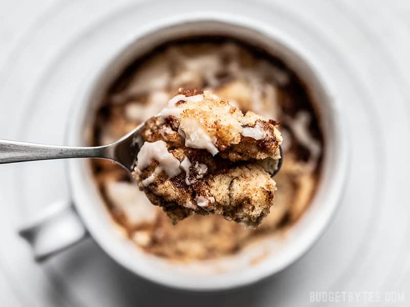 This Cinnamon Nut Swirl Mug Cake is the perfect way to get a single serving cinnamon roll fix without any kneading, rising, rolling, or baking! Budgetbytes.com Overhead view of a close up spoonful of Cinnamon Nut Swirl Mug Cake with the full mug in the background