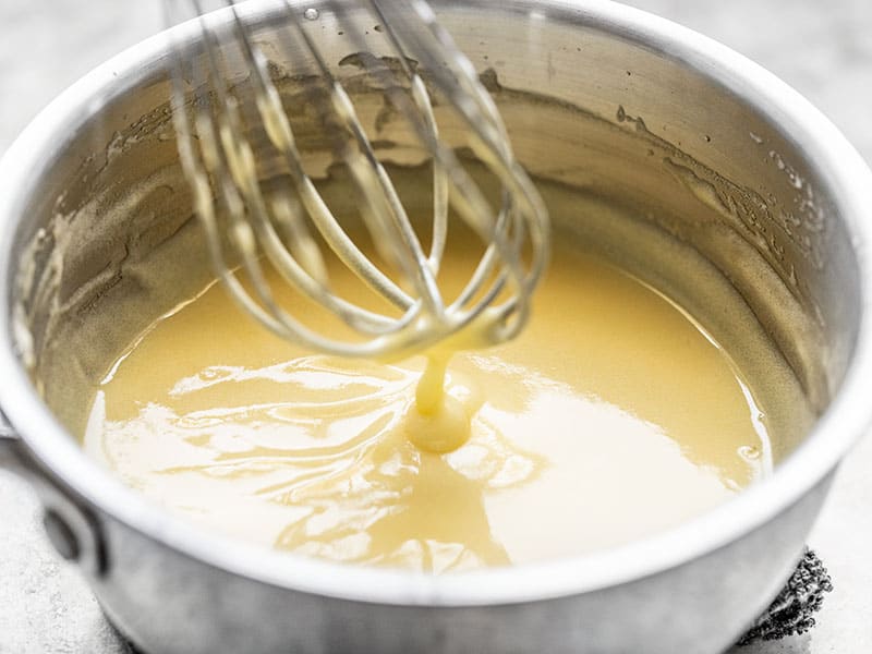 Finished lemon curd dripping off the whisk into the sauce pot.