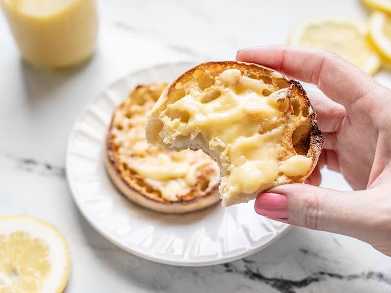 This luscious homemade lemon curd only takes four simple ingredients, about 10 minutes, and tastes like velvet sunshine in a jar. Budgetbytes.com A hand holding an English muffin smeared with homemade lemon curd, a bite is taken out of the muffin.