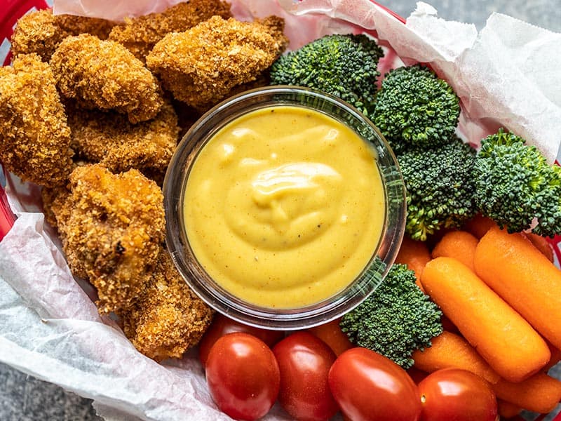 This sweet, tangy, and creamy homemade honey mustard sauce only takes a few minutes to make and is great for sandwiches, salads, dipping, and more! Budgetbytes.com Honey mustard sauce in a dish in the middle of a basket of chicken nuggets and vegetables.