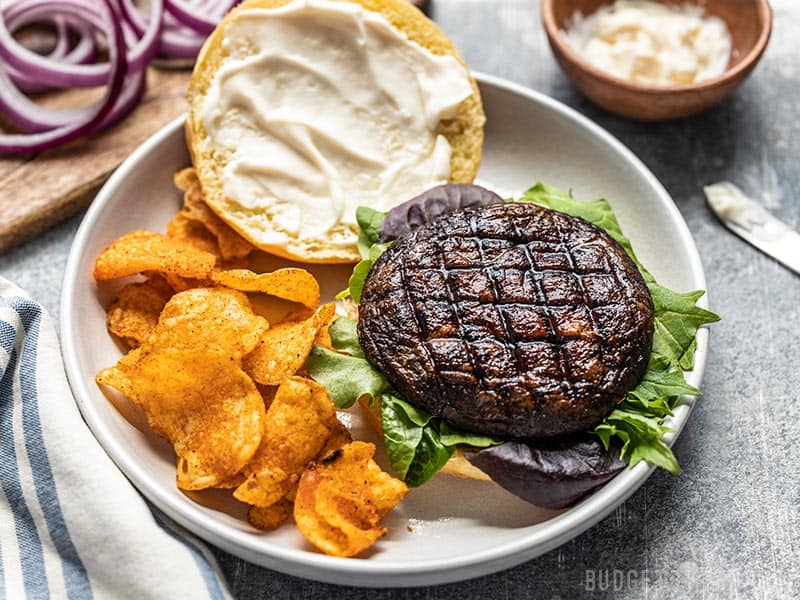 With their deep savory flavor, Marinated Portobello Mushroom Burgers are a fast and easy vegetarian option for summer grilling. Budgetbytes.com An open marinated portobello mushroom burger on a plate with chips, viewed from the front.
