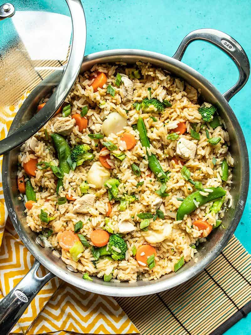 This One Pot Teriyaki Chicken and Rice is an easy and satisfying meal that the whole family will love. It also meal preps well for lunches all week! Budgetbytes.com Finished skillet full of One Pot Teriyaki Chicken and rice garnished with green onion, the skillet lid resting on the side.