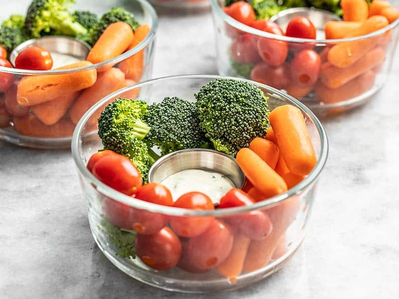 Make healthy snacking fast, easy, and hard to ignore with pre-packed veggie snack packs! Change up the vegetables and dressing each week for variety. Budgetbytes.com Front view of glass bowl veggie snack packs with ranch dressing, broccoli, carrots, and tomatoes.