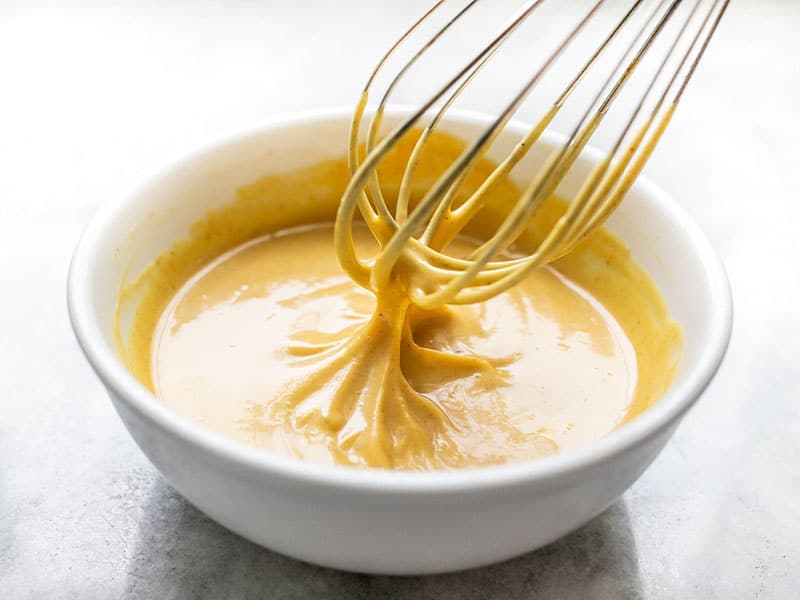This sweet, tangy, and creamy homemade honey mustard sauce only takes a few minutes to make and is great for sandwiches, salads, dipping, and more! Budgetbytes.com Whisked honey mustard sauce in a bowl with the whisk lifting out of the sauce.