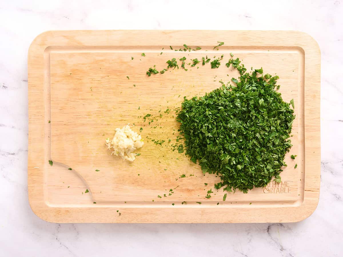 Chopped herbs and minced garlic on a cutting board.