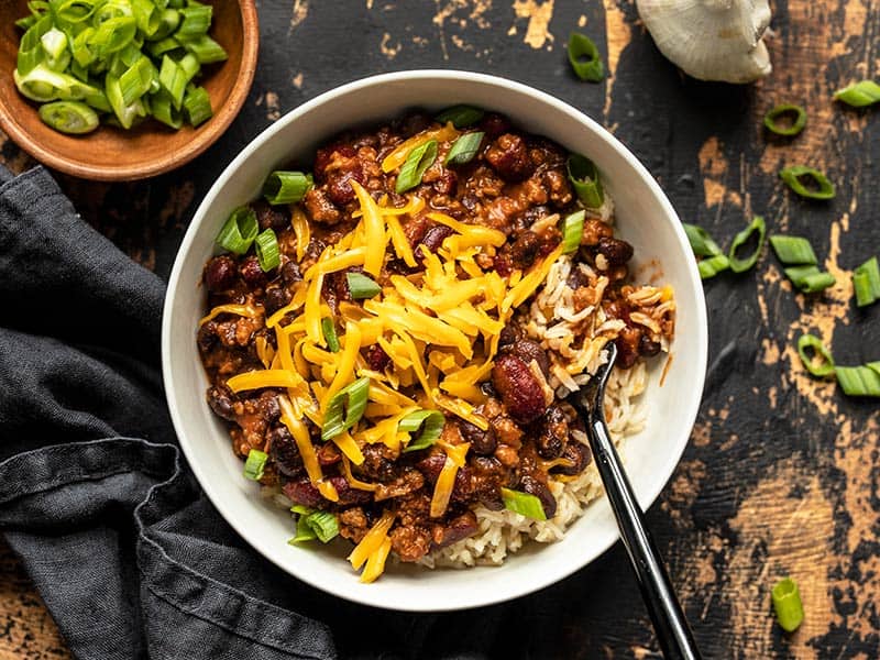 Serve these sweet, tangy, and savory BBQ Beef and Beans with rice and cheese for a simple and comforting weeknight dinner the whole family will love. Budgetbytes.com Overhead view of a bowl full of BBQ Beef and Beans, served with rice and topped with cheddar and green onion. A bowl of green onion on the side.