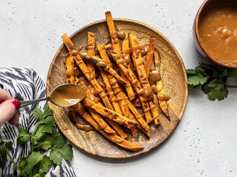 Peanut Lime Dressing being drizzled over baked sweet potato fries