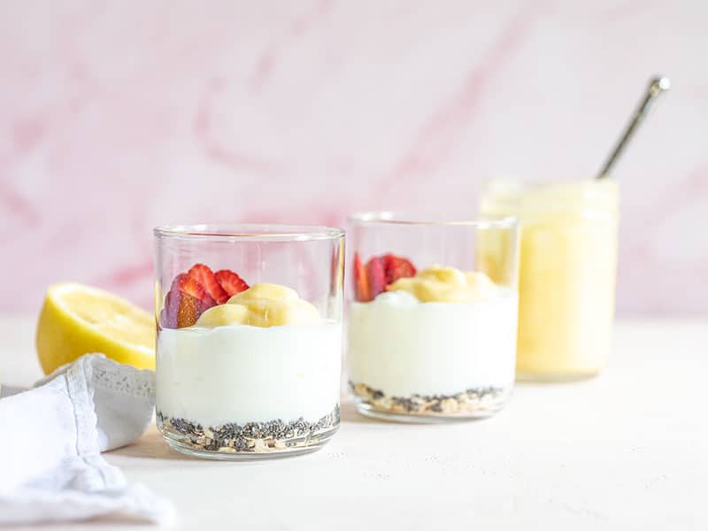 Creamy yogurt and bright, citrusy lemon curd make a dreamy base for these Lemon Berry Yogurt Breakfast bowls. A few oats, chia seeds and berries make it complete. Budgetbytes.com Two glasses filled with the lemon berry yogurt breakfast bowl ingredients, viewed from the side.