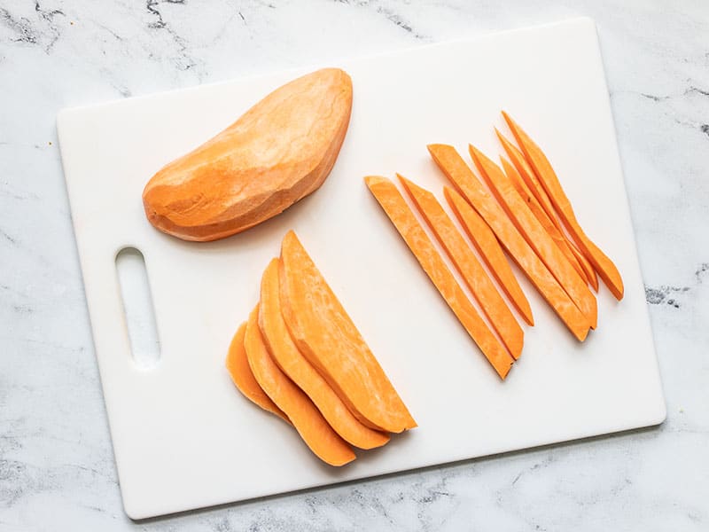 A peeled sweet potato being sliced into fries.