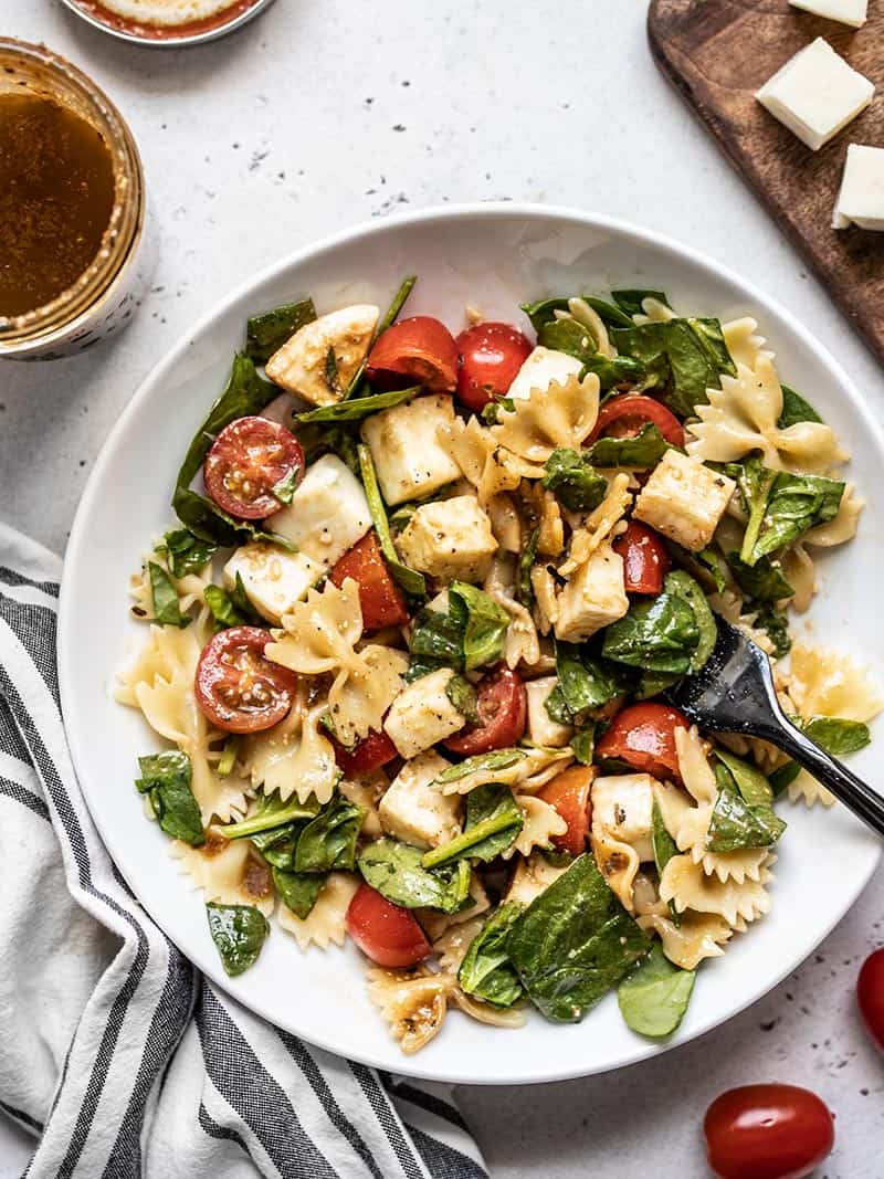 This Tomato Mozzarella Pasta Salad with homemade Parmesan Balsamic Vinaigrette is the perfect light and fresh summer meal. Perfect for potlucks! Budgetbytes.com A big bowl of Tomato Mozzarella Pasta Salad with a jar of dressing and cubed mozzarella on the sides.