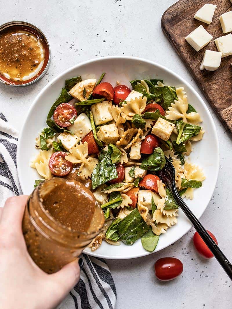 This Tomato Mozzarella Pasta Salad with homemade Parmesan Balsamic Vinaigrette is the perfect light and fresh summer meal. Perfect for potlucks! Budgetbytes.com Dressing being poured onto a bowl of tomato mozzarella pasta salad.