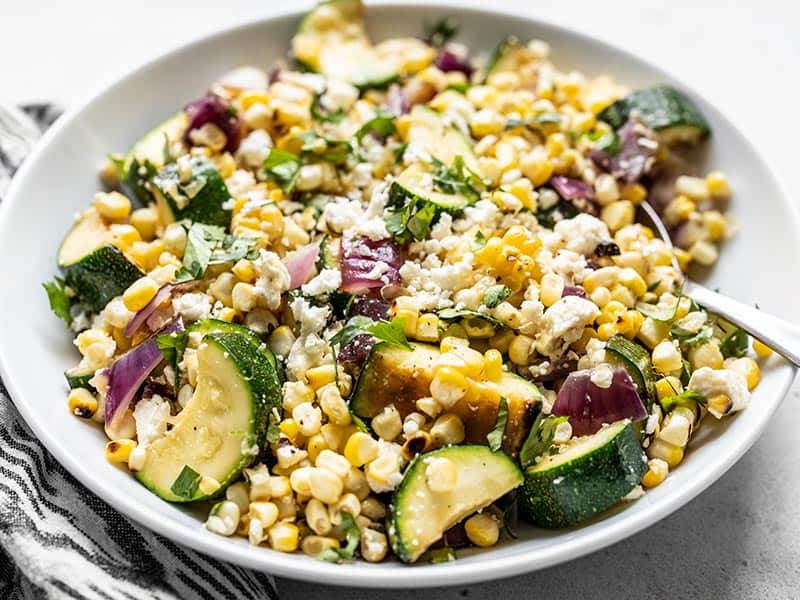 This Charred Corn and Zucchini Salad perfectly captures the flavor of summer with fresh sweet corn, salty feta, and a smoky grill-like flavor. BudgetBytes.com Front view of a large bowl full of Charred Corn and Zucchini Salad topped with crumbled feta and cilantro