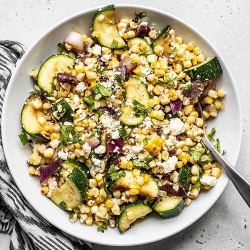 Overhead view of a bowl of Charred Corn and Zucchini Salad with a black and white napkin on the side.