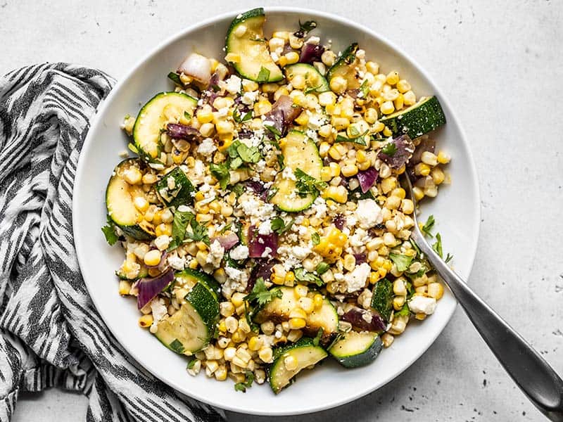 This Charred Corn and Zucchini Salad perfectly captures the flavor of summer with fresh sweet corn, salty feta, and a smoky grill-like flavor. BudgetBytes.com Overhead view of a bowl of Charred Corn and Zucchini Salad with a black and white napkin on the side.