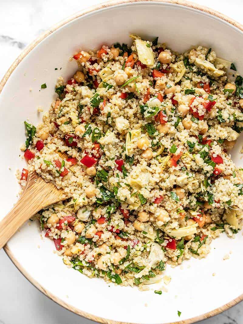 This Lemony Artichoke and Quinoa Salad is a light and refreshing summer salad that holds up well in the refrigerator and is perfect for meal prep! BudgetBytes.com Close up of finished Lemony Artichoke and Quinoa Salad in the mixing bowl with wooden salad tongs
