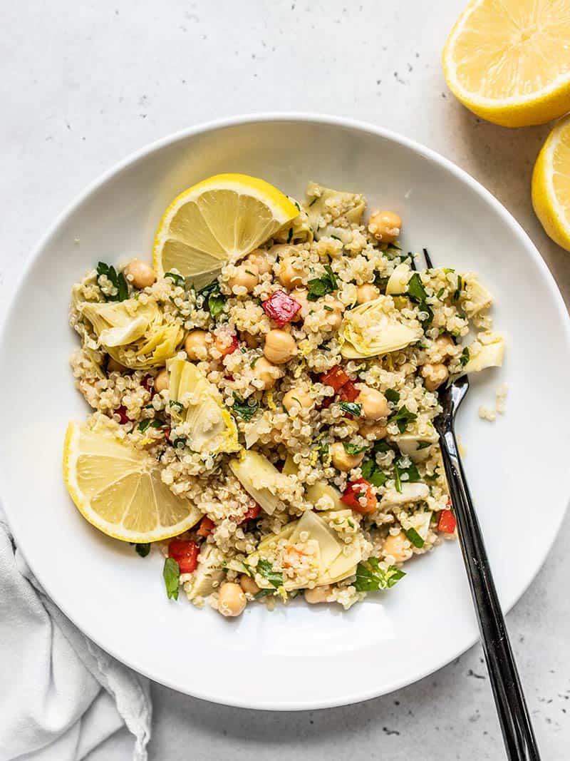 This Lemony Artichoke and Quinoa Salad is a light and refreshing summer salad that holds up well in the refrigerator and is perfect for meal prep! BudgetBytes.com Overhead view of a bowl of Lemony Artichoke and Quinoa Salad with lemon wedges and a black fork.