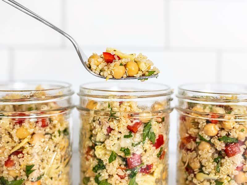 This Lemony Artichoke and Quinoa Salad is a light and refreshing summer salad that holds up well in the refrigerator and is perfect for meal prep! BudgetBytes.com Lemony Artichoke and Quinoa Salad in mason jars, a forkful hovering above.